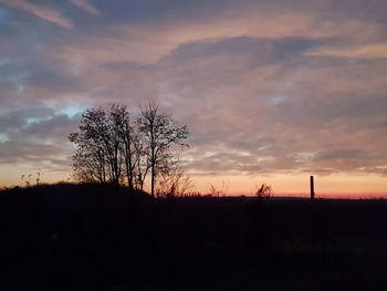 Silhouette bare trees on landscape against sky at sunset