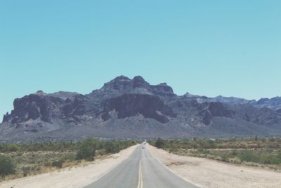 Empty road by mountains against clear blue sky