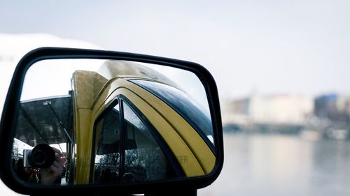 Reflection of bus in side-view mirror against sky