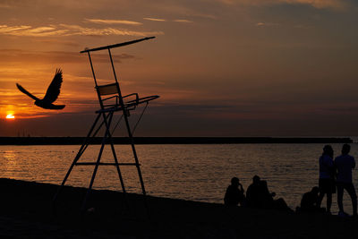 Silhouette people on beach against sky during sunset