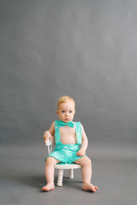 A one-year-old boy is sitting on a white children's chair on a gray background. copy space