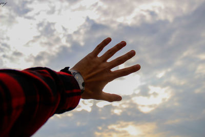 Cropped hand of man reaching cloudy sky during sunset