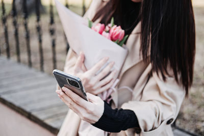 Spring outdoor portrait of happy woman with tulips bouquet, smartphone and coffee to go on spring