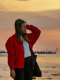 Young woman looking away while standing at beach during sunset