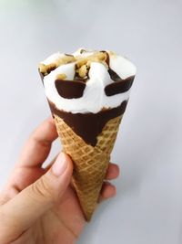 Close-up of hand holding ice cream cone against white background