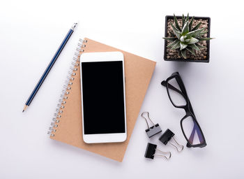 Directly above shot of mobile phone on spiral notebook by eyeglasses on table