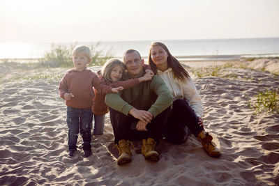 Family with a son and daughter and a dog sit on the sand in autumn