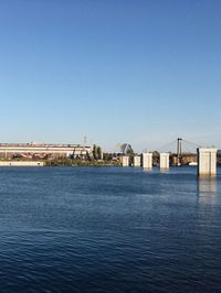 Bridge over sea against buildings against clear blue sky