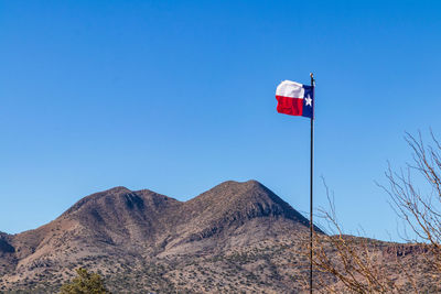 Low angle view of flag against mountain range against blue sky