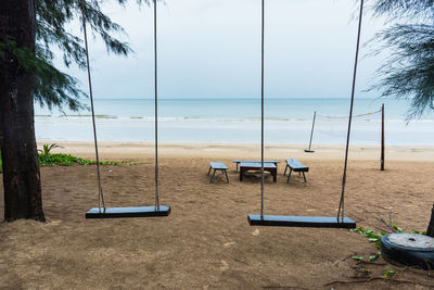 Empty swings at shore of beach against sky