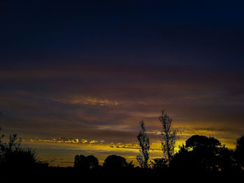 Silhouette trees on field against sky at sunset