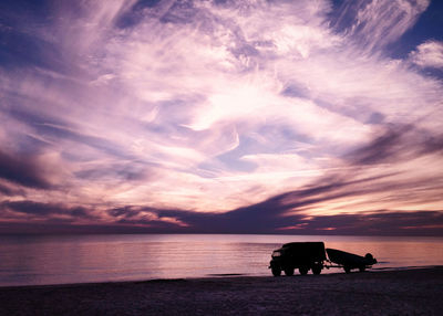 Silhouette dog on beach against sky during sunset