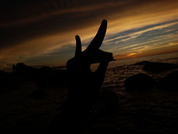 Silhouette hand against sky during sunset