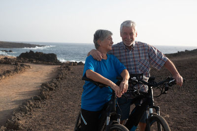 Smiling couple talking while standing with bicycles against sea