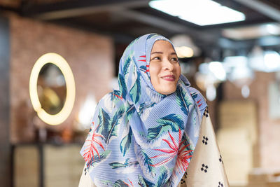 Smiling woman in hijab looking away at cafe