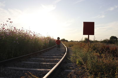 Girl running on railroad tracks against sky during sunset