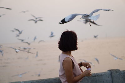 Side view of woman looking at seagulls flying at beach