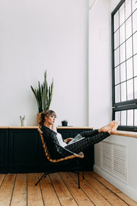 Girl in a business suit and glasses stands working near the window at home, in the office