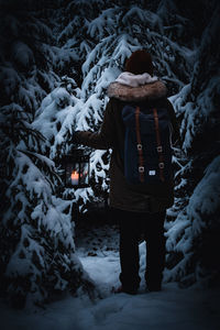 Person carrying lantern and backpack in winterly forest