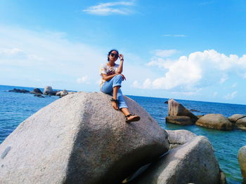 Young woman sitting on retaining wall by sea against sky