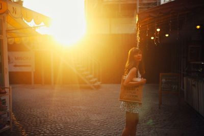 Side view of woman standing on street during sunset
