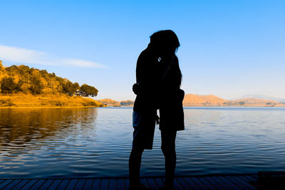 Silhouette man standing by lake against sky