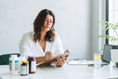 Young smiling brunette woman doctor nutritionist working at laptop at modern bright office 