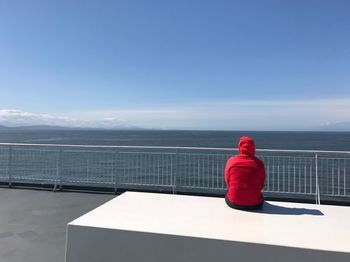 Rear view of woman sitting by railing against sea and sky