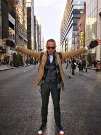 Full length of man with arms outstretched standing on road in city