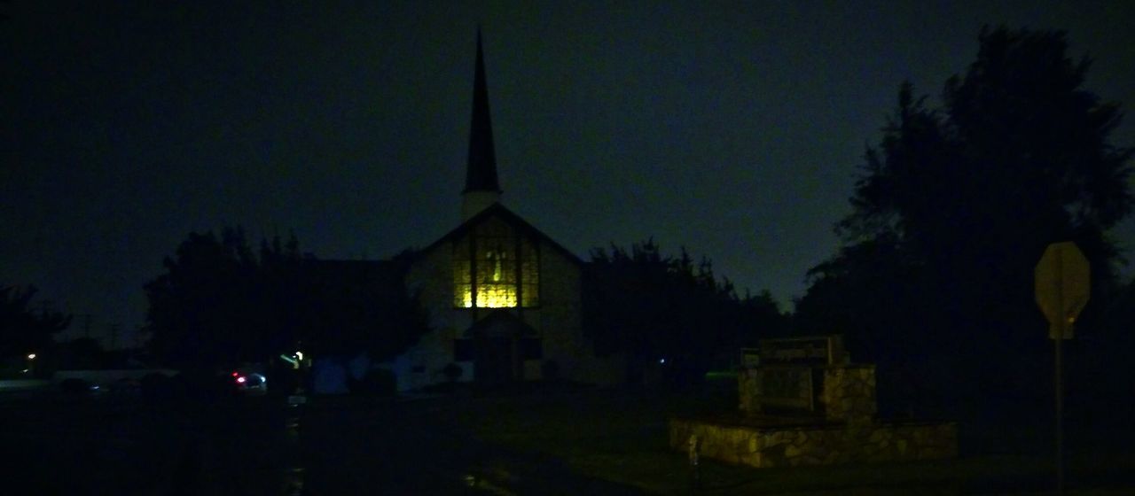 night, religion, building exterior, illuminated, church, architecture, place of worship, built structure, spirituality, sky, low angle view, cathedral, tree, dark, dusk, cross, outdoors, silhouette