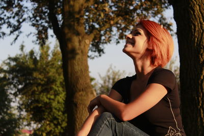 Young woman looking away while sitting on tree