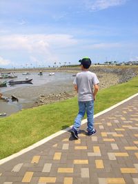 Rear view of boy walking on road by river against sky