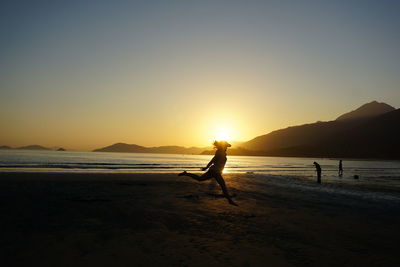 Silhouette people on beach against clear sky during sunset