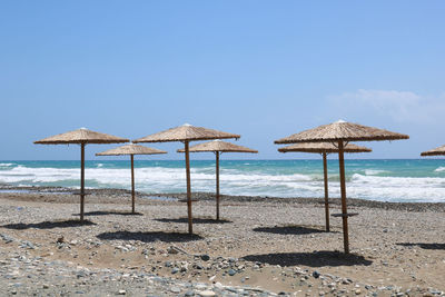 Empty pebble beach with straw umbrellas in front of the sea