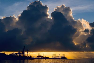 Silhouette cranes at commercial dock against sky during sunrise 