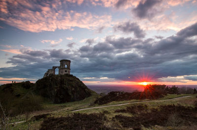 Scenic view of landscape against cloudy sky at sunset