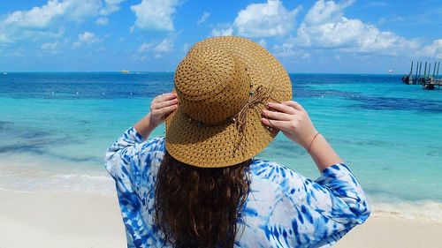 Rear view of woman in hat standing at beach against sky