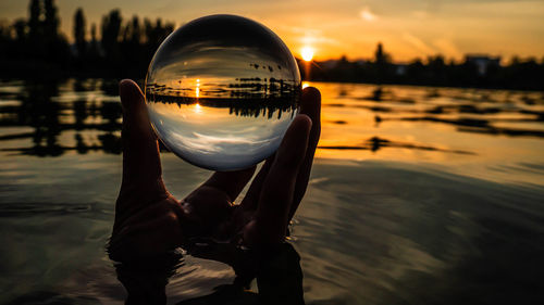 Close-up of person holding crystal ball in city at sunset