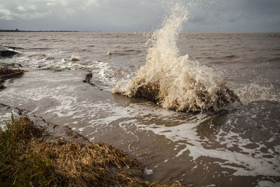 Waves splashing on shore against sky