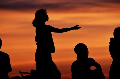 Silhouette people on beach against orange sky