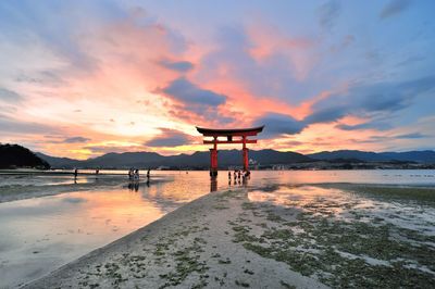 Torii gate in sea at itsukushima shrine against sky during sunset