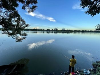 Rear view of man standing by lake against sky