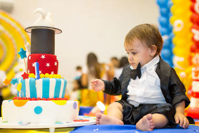 Close-up of cute baby boy sitting by birthday cake