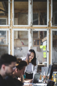 Confident female it professional looking at colleague coding in laptop at workplace