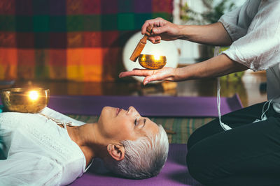 Midsection of woman playing singing bowl for customer in spa