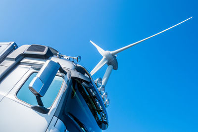 Low angle view of truck and wind turbine against clear blue sky