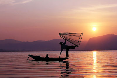 Silhouette people on boat in lake against sky during sunset