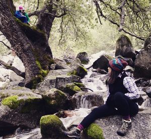 Rear view of woman sitting on rock in forest