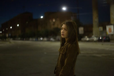 Side view of young woman looking at illuminated city street
