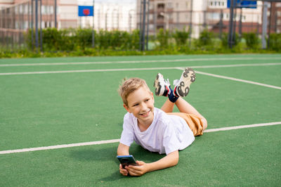 The boy is lying on the floor and playing with the phone